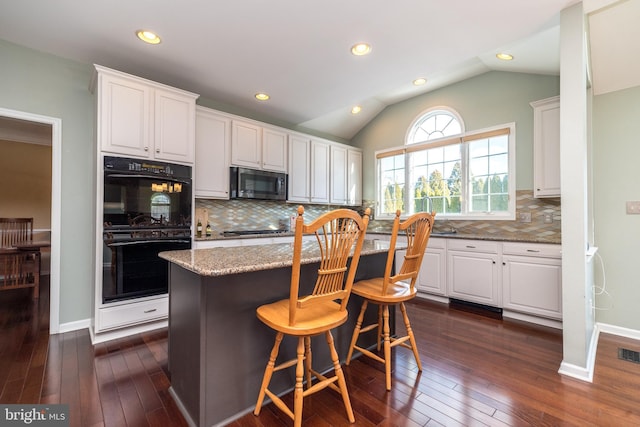 kitchen featuring white cabinetry, double oven, stone countertops, vaulted ceiling, and a kitchen bar