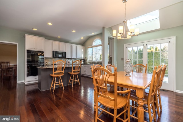 dining room featuring vaulted ceiling with skylight, sink, dark wood-type flooring, and an inviting chandelier