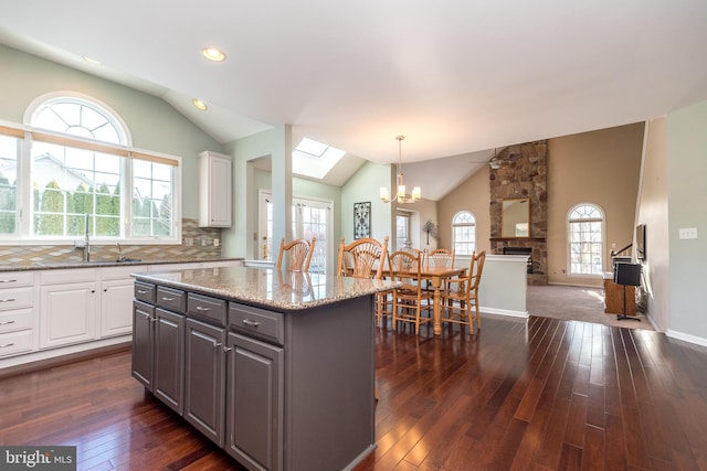 kitchen with backsplash, white cabinets, sink, hanging light fixtures, and light stone countertops