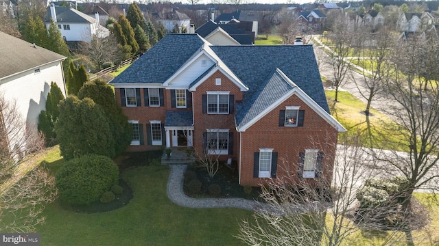 view of front of property featuring a shingled roof, brick siding, and a front lawn