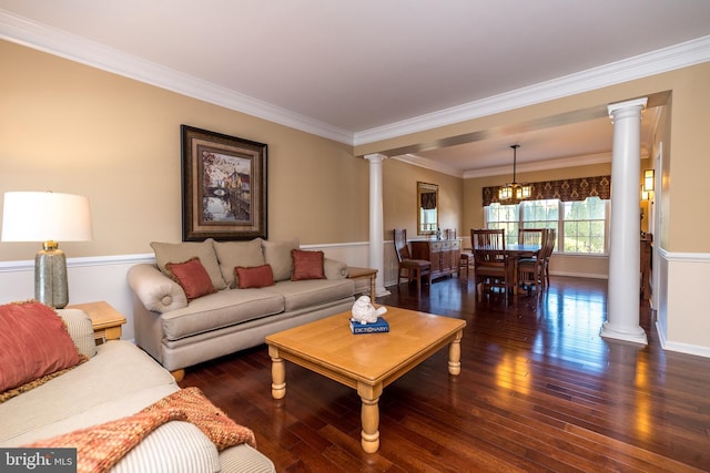 living room featuring dark hardwood / wood-style floors, an inviting chandelier, ornamental molding, and ornate columns