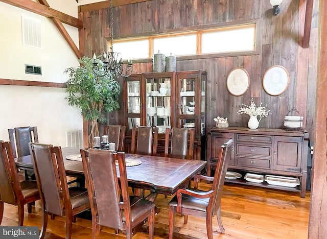 dining area with a chandelier, a high ceiling, light wood-type flooring, and wooden walls