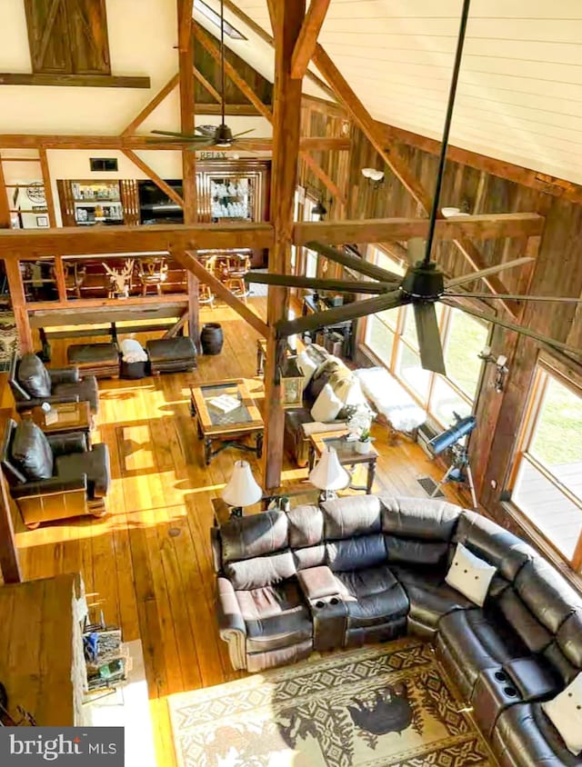 living room with lofted ceiling with beams, hardwood / wood-style flooring, ceiling fan, and wood walls