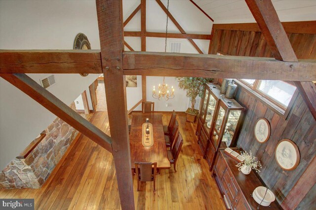 stairs with high vaulted ceiling, an inviting chandelier, wooden walls, hardwood / wood-style flooring, and beam ceiling