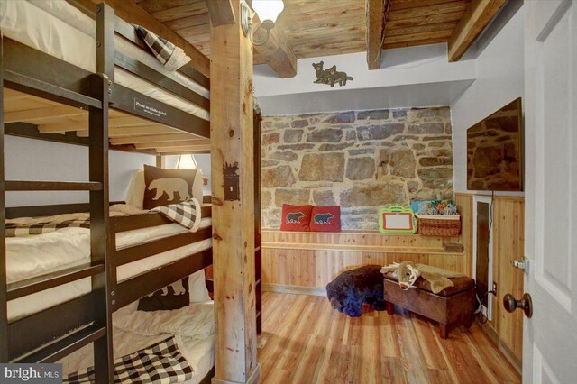 bedroom with beamed ceiling, hardwood / wood-style flooring, wooden ceiling, and wood walls