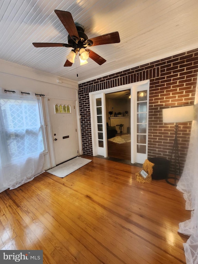 interior space with hardwood / wood-style flooring, ceiling fan, wooden ceiling, and brick wall