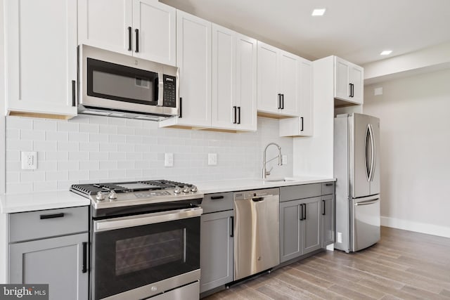 kitchen featuring gray cabinetry, white cabinets, sink, light wood-type flooring, and appliances with stainless steel finishes