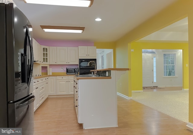 kitchen with white cabinetry, a kitchen island with sink, black refrigerator with ice dispenser, and light hardwood / wood-style flooring