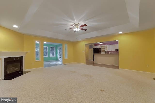 unfurnished living room with a raised ceiling, a premium fireplace, carpet floors, and ceiling fan