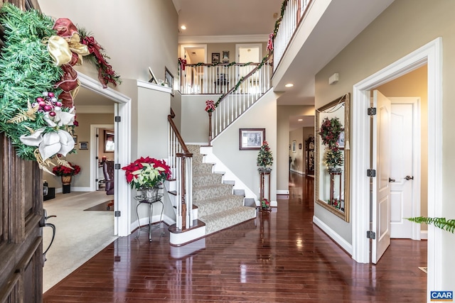 entryway with dark colored carpet, a towering ceiling, and crown molding