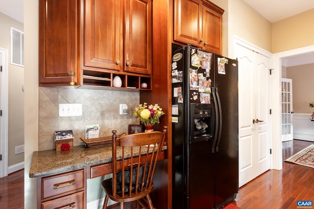 kitchen with stone counters, dark hardwood / wood-style floors, backsplash, black fridge with ice dispenser, and built in desk