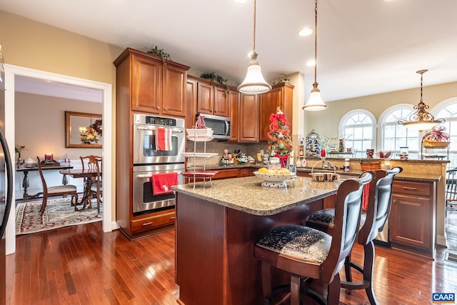 kitchen featuring pendant lighting, dark wood-type flooring, tasteful backsplash, light stone counters, and stainless steel appliances