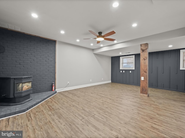 basement with light wood-type flooring, a wood stove, and ceiling fan