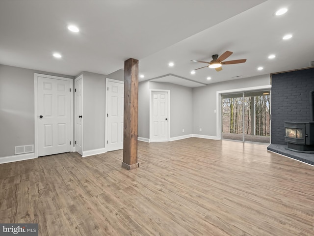 unfurnished living room with light hardwood / wood-style floors, a wood stove, and ceiling fan