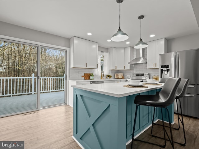 kitchen with a wealth of natural light, white cabinetry, stainless steel appliances, and wall chimney range hood