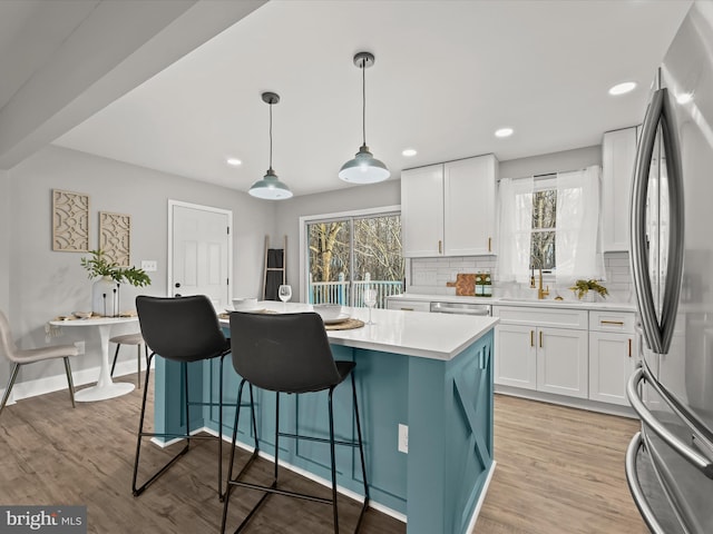 kitchen featuring white cabinets, stainless steel fridge, decorative light fixtures, and light hardwood / wood-style floors