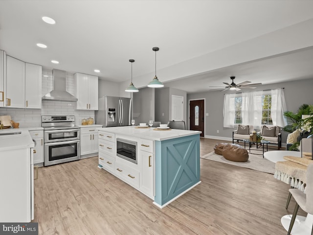 kitchen with a center island, wall chimney range hood, light wood-type flooring, white cabinetry, and stainless steel appliances