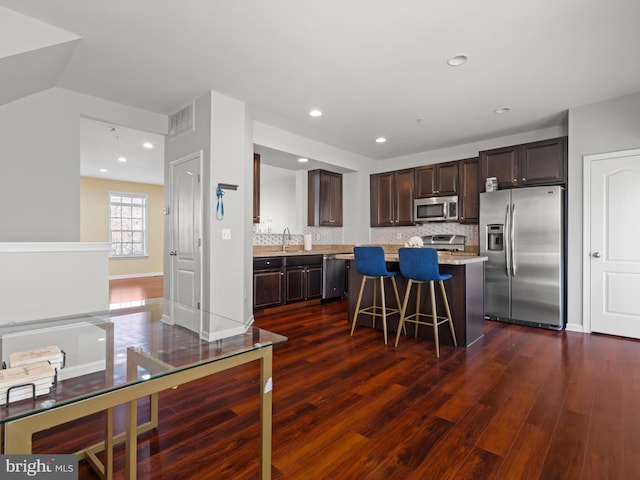 kitchen with a kitchen bar, backsplash, appliances with stainless steel finishes, a kitchen island, and dark hardwood / wood-style flooring