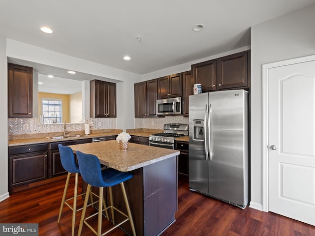 kitchen with a kitchen bar, a center island, dark hardwood / wood-style floors, and appliances with stainless steel finishes