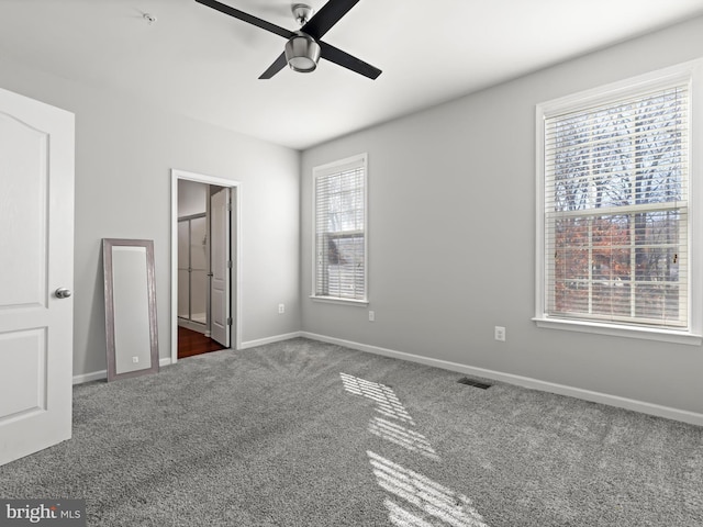 unfurnished bedroom featuring ensuite bathroom, dark carpet, and ceiling fan