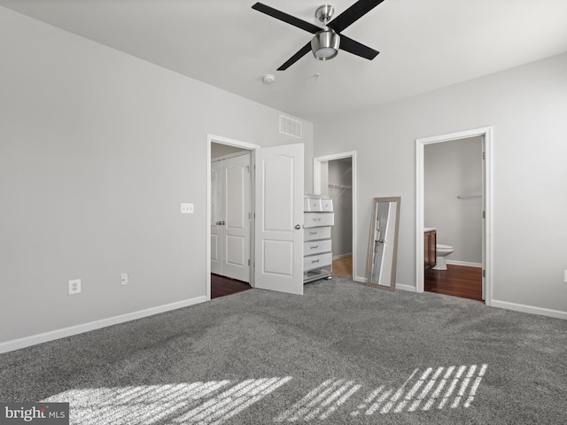 unfurnished bedroom featuring connected bathroom, ceiling fan, a walk in closet, a closet, and dark carpet