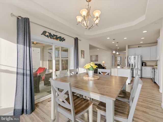 dining room featuring an inviting chandelier, a raised ceiling, sink, and light hardwood / wood-style flooring