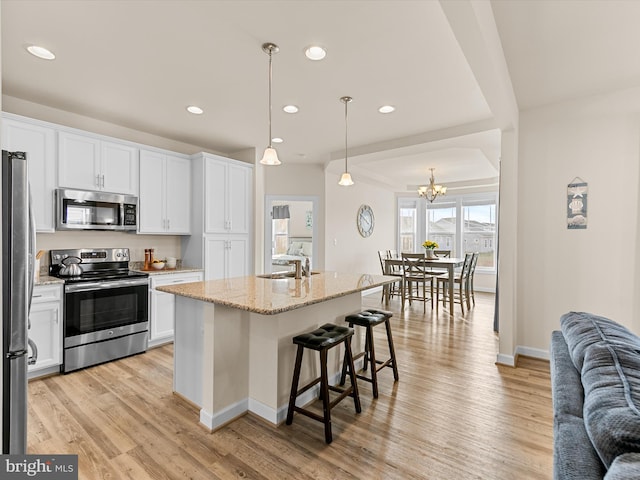 kitchen featuring white cabinets, appliances with stainless steel finishes, a kitchen island with sink, and pendant lighting