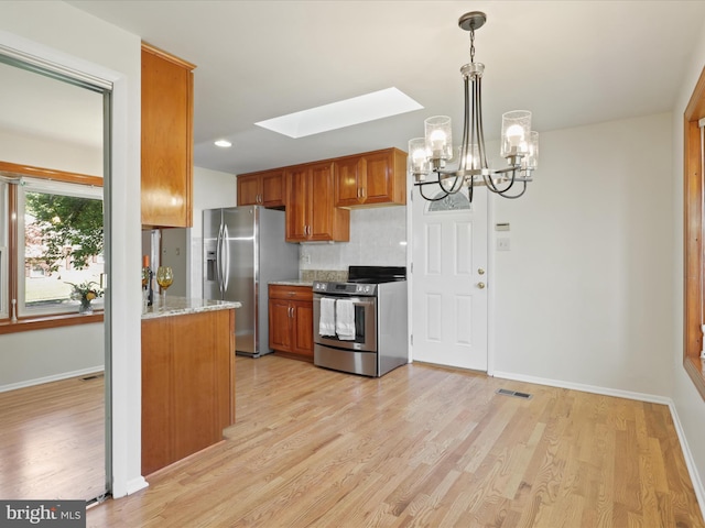 kitchen with a skylight, stainless steel appliances, an inviting chandelier, light stone counters, and light hardwood / wood-style floors