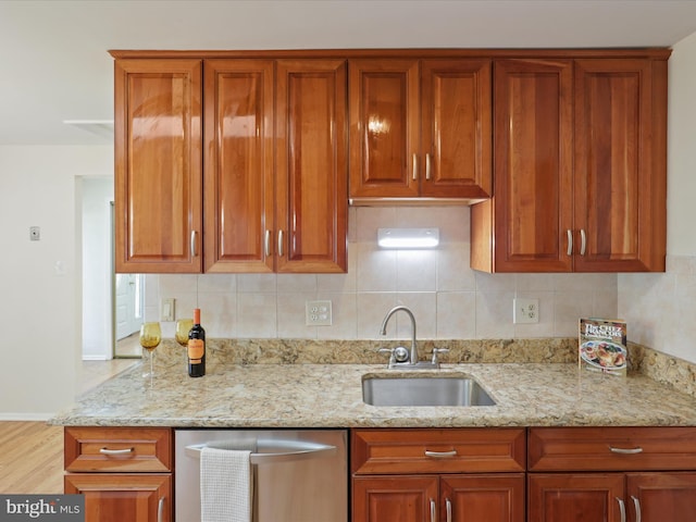 kitchen with light stone countertops, sink, stainless steel dishwasher, light hardwood / wood-style floors, and decorative backsplash