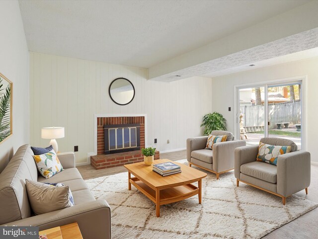 living room featuring wood walls, light wood-type flooring, a textured ceiling, and a brick fireplace