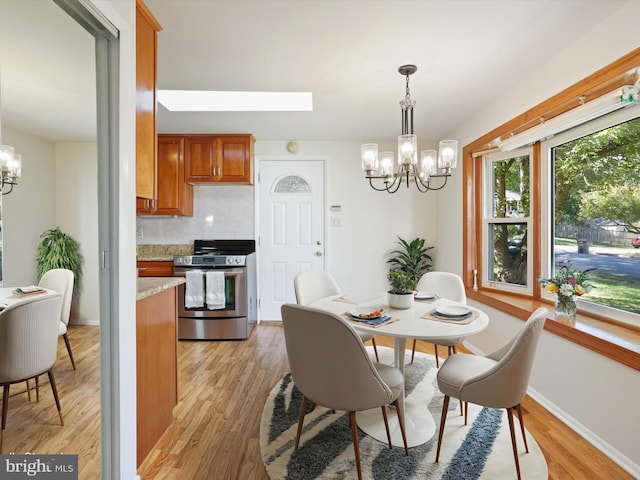 dining space with light hardwood / wood-style floors, a skylight, and an inviting chandelier