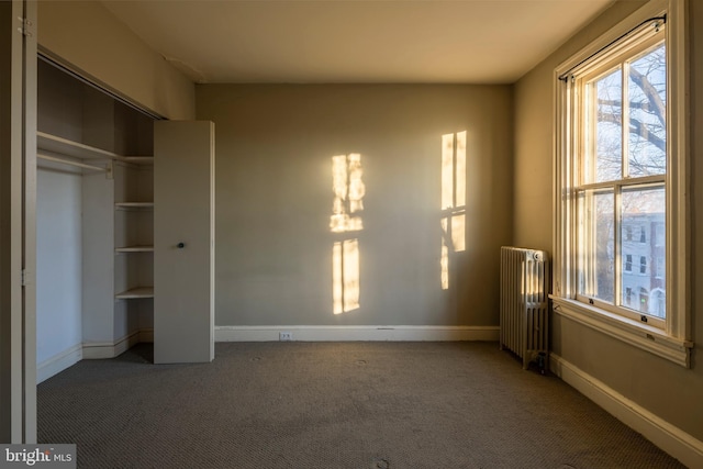 unfurnished bedroom featuring dark colored carpet, radiator heating unit, and a closet