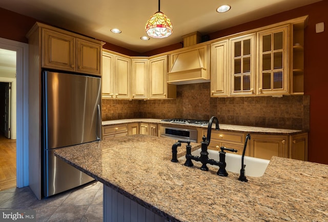 kitchen featuring custom exhaust hood, sink, appliances with stainless steel finishes, decorative light fixtures, and light stone counters