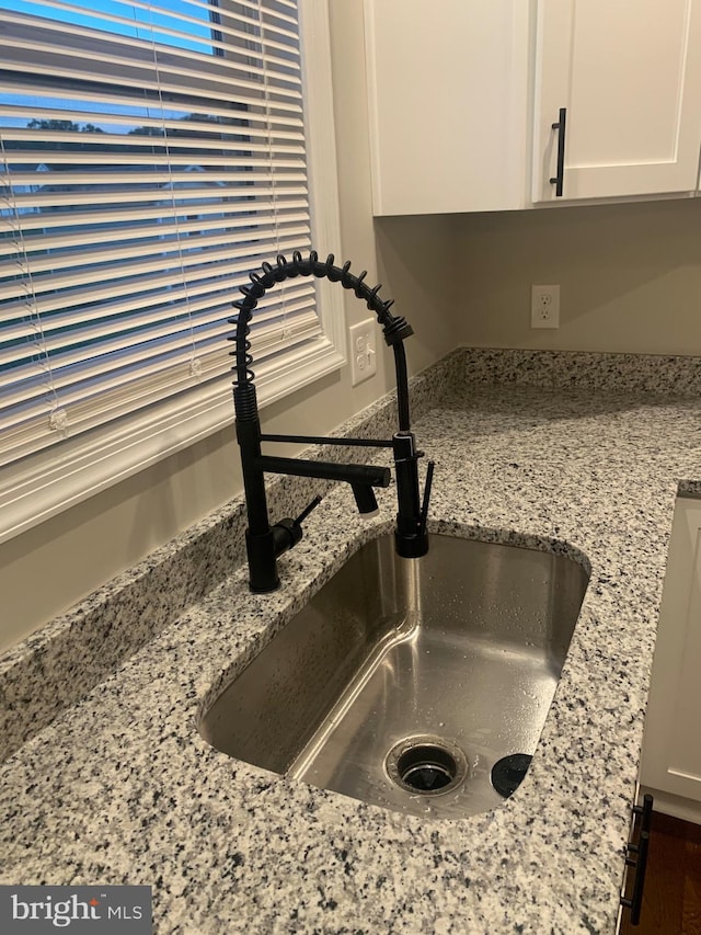 room details featuring white cabinets, light stone counters, and sink