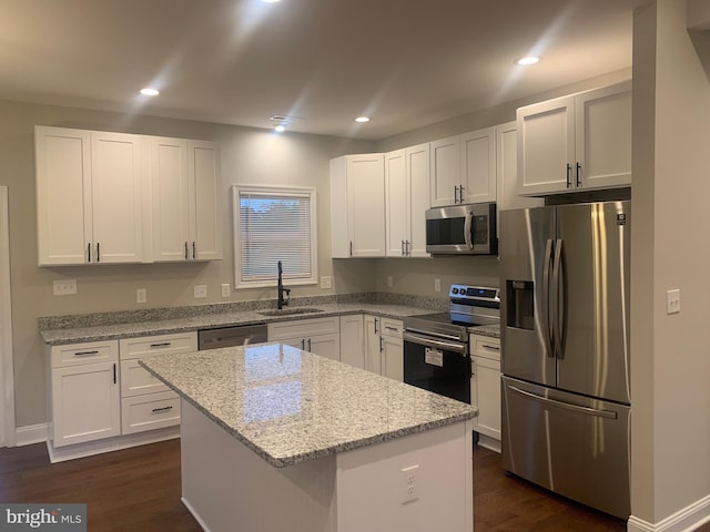 kitchen featuring appliances with stainless steel finishes, light stone counters, a kitchen island, sink, and white cabinetry