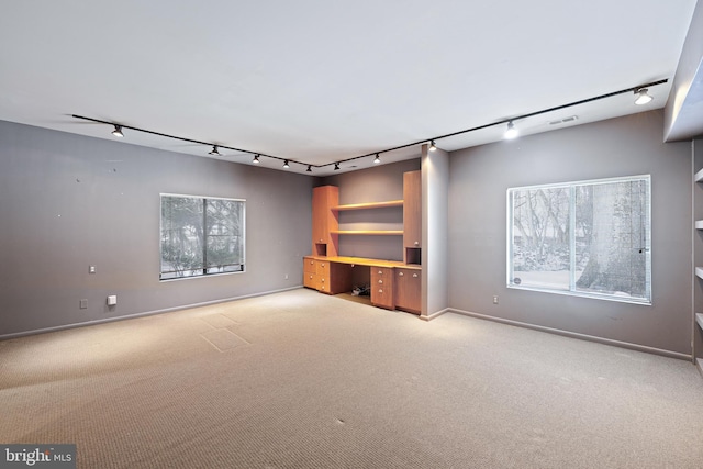 unfurnished living room with rail lighting, light colored carpet, and built in desk