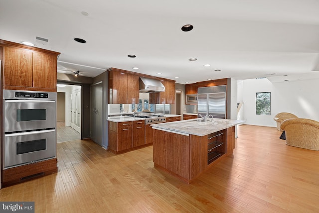 kitchen featuring wall chimney exhaust hood, built in appliances, a center island, and light hardwood / wood-style floors