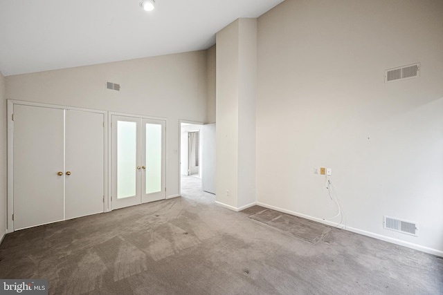 carpeted empty room with high vaulted ceiling and french doors