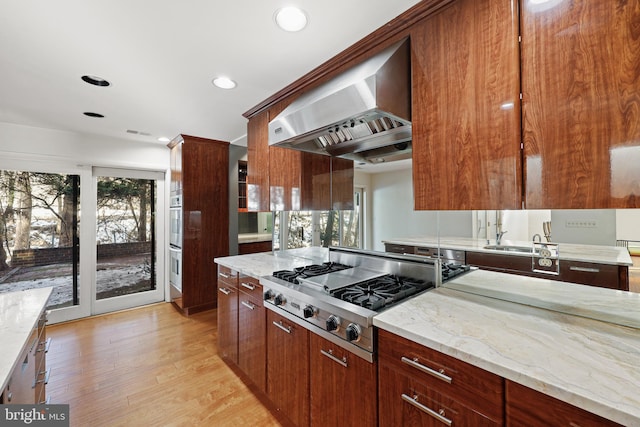 kitchen featuring stainless steel appliances, light stone countertops, a wealth of natural light, and wall chimney exhaust hood