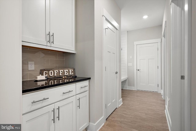 bar with white cabinetry, light hardwood / wood-style flooring, and backsplash