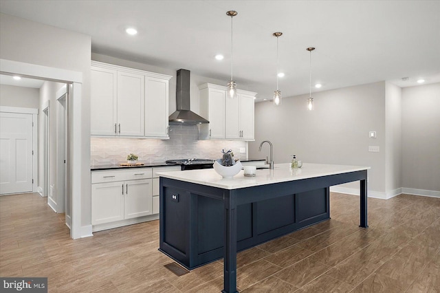 kitchen featuring decorative light fixtures, white cabinets, wall chimney exhaust hood, and a center island with sink