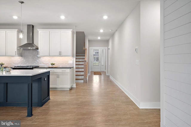 kitchen with pendant lighting, white cabinetry, wall chimney exhaust hood, and tasteful backsplash