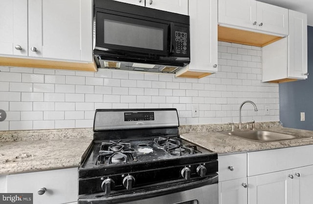 kitchen with stainless steel range with gas cooktop, tasteful backsplash, white cabinetry, sink, and light stone counters