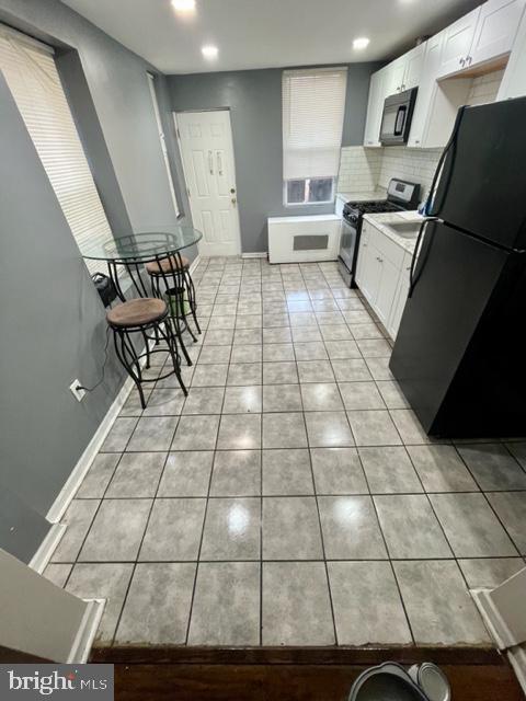 kitchen featuring white cabinetry, light tile patterned floors, tasteful backsplash, and black appliances