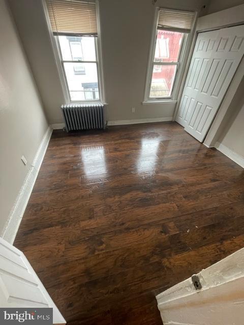 unfurnished bedroom featuring a closet, dark hardwood / wood-style flooring, radiator, and multiple windows