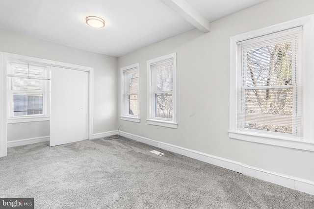 unfurnished bedroom featuring beam ceiling, carpet floors, and multiple windows