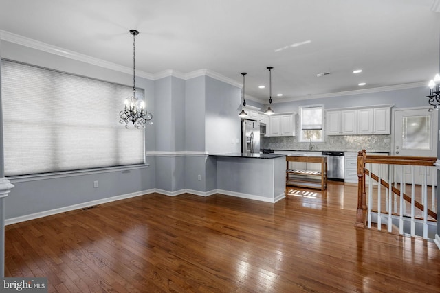 kitchen featuring dark hardwood / wood-style floors, ornamental molding, appliances with stainless steel finishes, decorative light fixtures, and white cabinetry