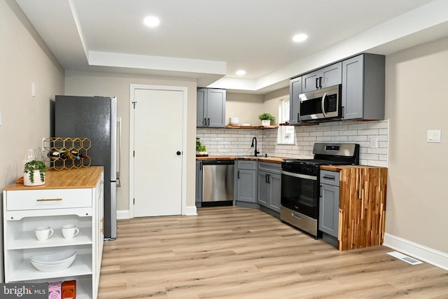 kitchen with open shelves, appliances with stainless steel finishes, wooden counters, gray cabinetry, and a sink