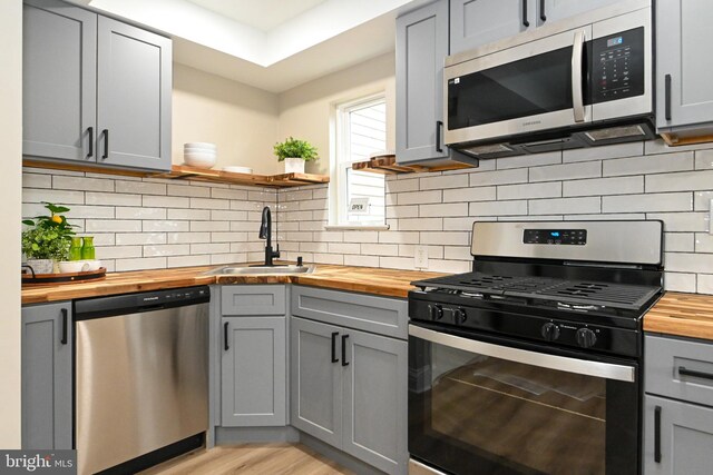 kitchen featuring wood counters, appliances with stainless steel finishes, gray cabinets, open shelves, and a sink