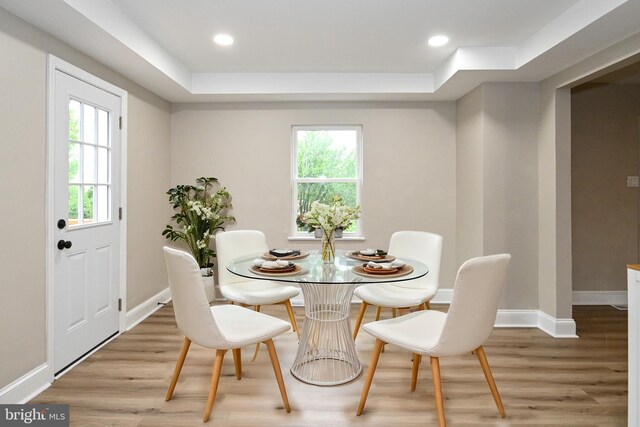 dining area featuring light wood-style flooring, baseboards, a raised ceiling, and recessed lighting